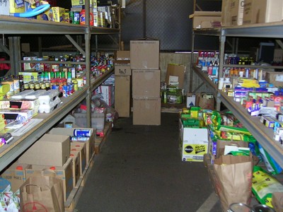An interior view of a storage room with shelves lined with various boxes and containers of food items, organized alongside cardboard boxes on the floor.