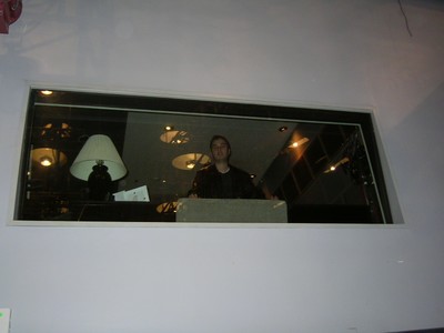 A person standing in a control room behind a glass window, with visible lights and a lamp in the background.