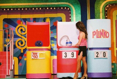 A contestant interacting with a game display featuring a Plinko board, against a colorful game show backdrop.