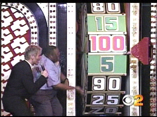 A game show host and contestant interacting with a large spinning wheel displaying various numbers during a special moment on The Price is Right.