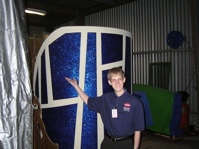 A person standing next to a large, glittery prop with geometric designs in a backstage area.