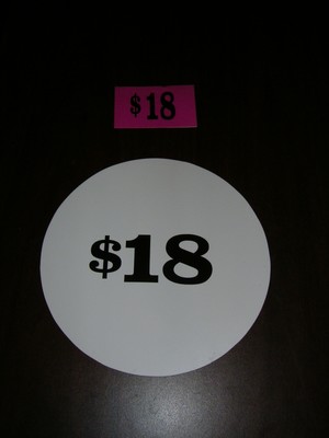 A round white sign with the number $18 printed in bold black text, placed beside a rectangular pink sign also displaying $18.
