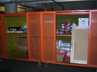 Storage unit with orange metal mesh doors, containing various items such as boxes, utensils, and packaging materials.