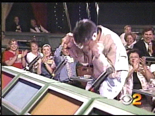 A contestant celebrating enthusiastically at a game show, with an audience applauding in the background.