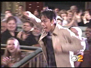 A man excitedly runs through a crowd on a game show set, with an audience cheering in the background.