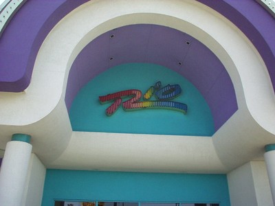 Exterior view of a colorful building entrance featuring a sign with the word 'Rio' in multicolored letters, set against a light blue and purple background.