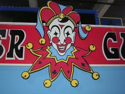Close-up of a colorful jester-like character logo with vibrant colors, featuring a smiling face and exaggerated features, set against a bright background.