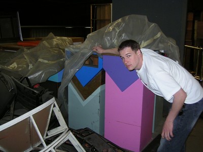 A person stands next to colorful display stands covered partially with plastic in a studio environment.