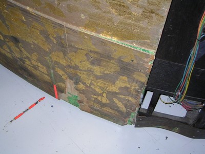 Close-up view of a weathered wooden surface with golden paint, showing wear and exposed layers, along with some wires and a bright orange object.