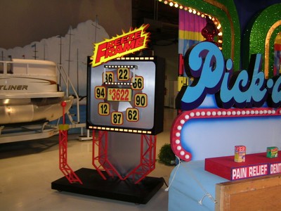 A colorful game display featuring a numbers board labeled 'Freeze Frame' with rotating numbers, alongside a 'Pick-a' sign in a vibrant setting.