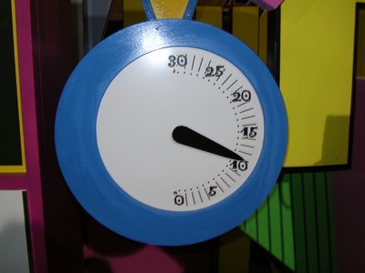 A close-up of a blue-framed timer used in Bonkers with a white face and black hands, positioned at around 10 seconds, set against a colorful backdrop.