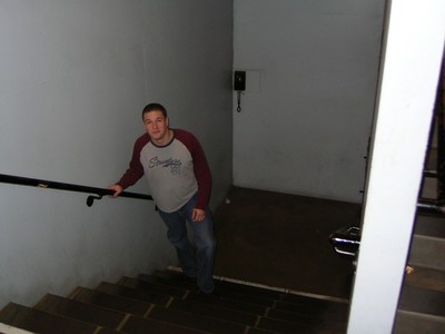 A person in casual clothing ascends a staircase with a railing in a dimly lit corridor.