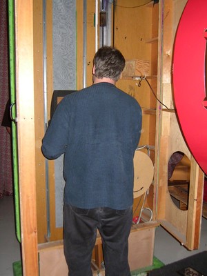 A person standing with their back to the camera, interacting with a game show structure in a storage area, surrounded by wooden panels and equipment.