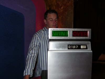 A game show host interacts with a prize indicator displaying 'WIN' and 'OVER' lights, with a visible score of 2187.