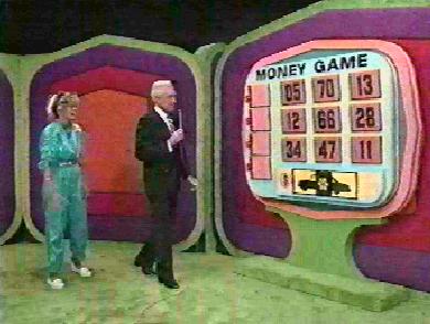 A contestant and host standing next to a game board during the Money Game segment on The Price is Right, featuring numbers displayed on a large screen.