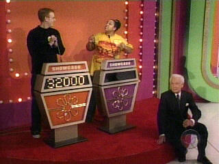 A scene from 'The Price is Right' featuring two contestants at showcase podiums and the host seated on the floor.