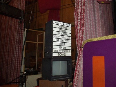A display board with game names such as 'Credit Card,' 'Dice Game,' 'Cliff Hangers,' and 'Showcase Showdown' mounted on a black structure in a studio setting.