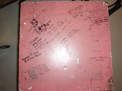 A worn pink board covered in various handwritten notes and markings, likely used for tracking information in a studio environment.