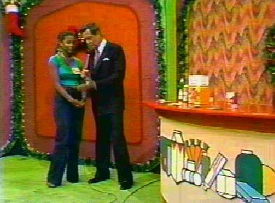 A scene from Grocery Game featuring a host and a contestant, standing together in front of a colorful set decorated for a festive occasion on The Price is Right.