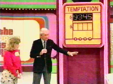 A host stands next to a game board labeled 'TEMPTATION' showing a number, while a contestant in a red shirt looks on.