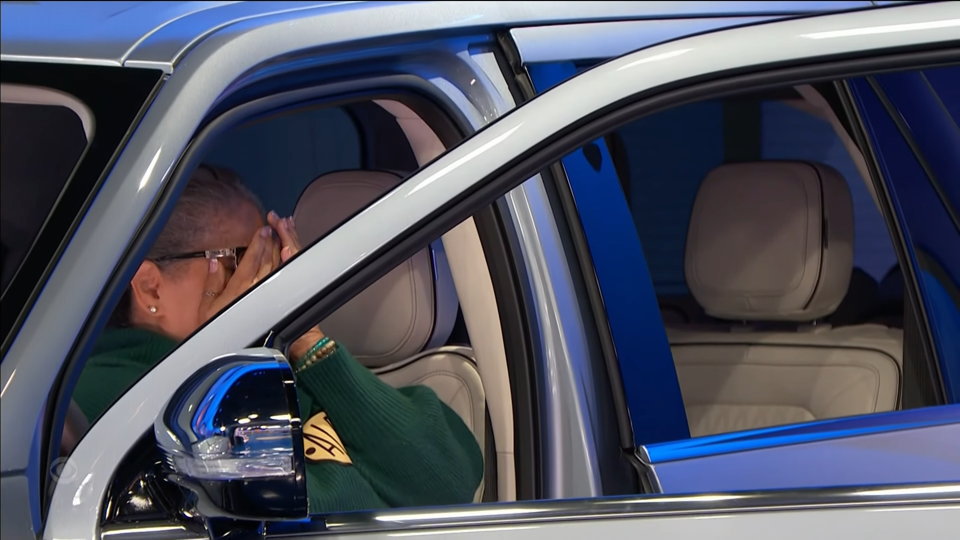 A contestant sitting inside a luxury SUV, covering her face with her hands, expressing a mix of disbelief and joy.