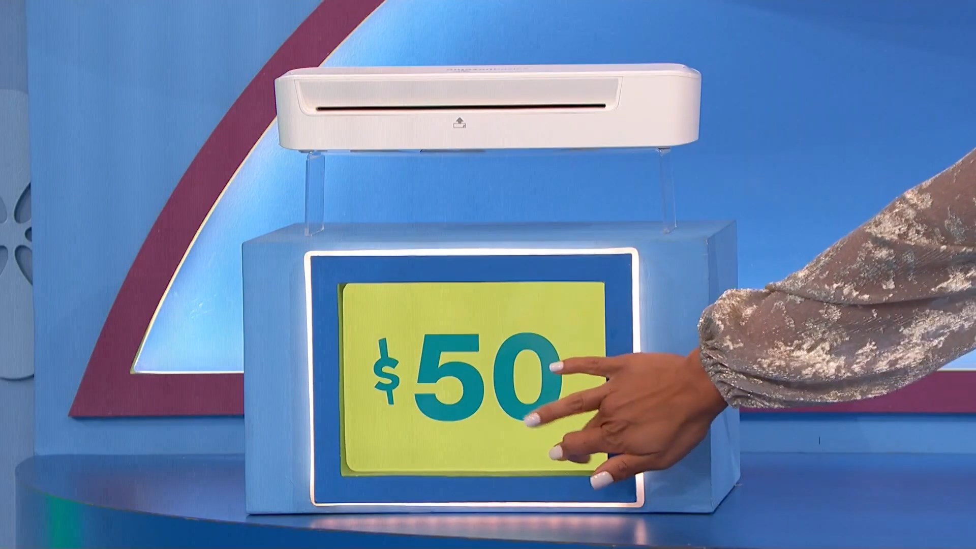 A game set piece from The Price is Right featuring a price tag of  next to a white device, with a contestant's hand pointing at the tag.