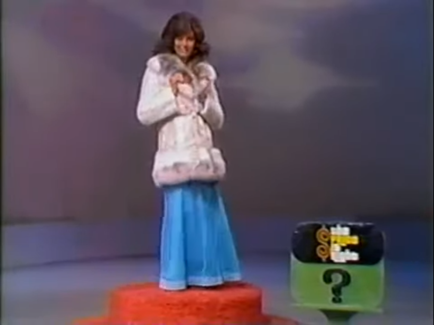 A woman wearing a stylish fur coat and a blue skirt stands on a red platform next to a price tag display with a question mark.