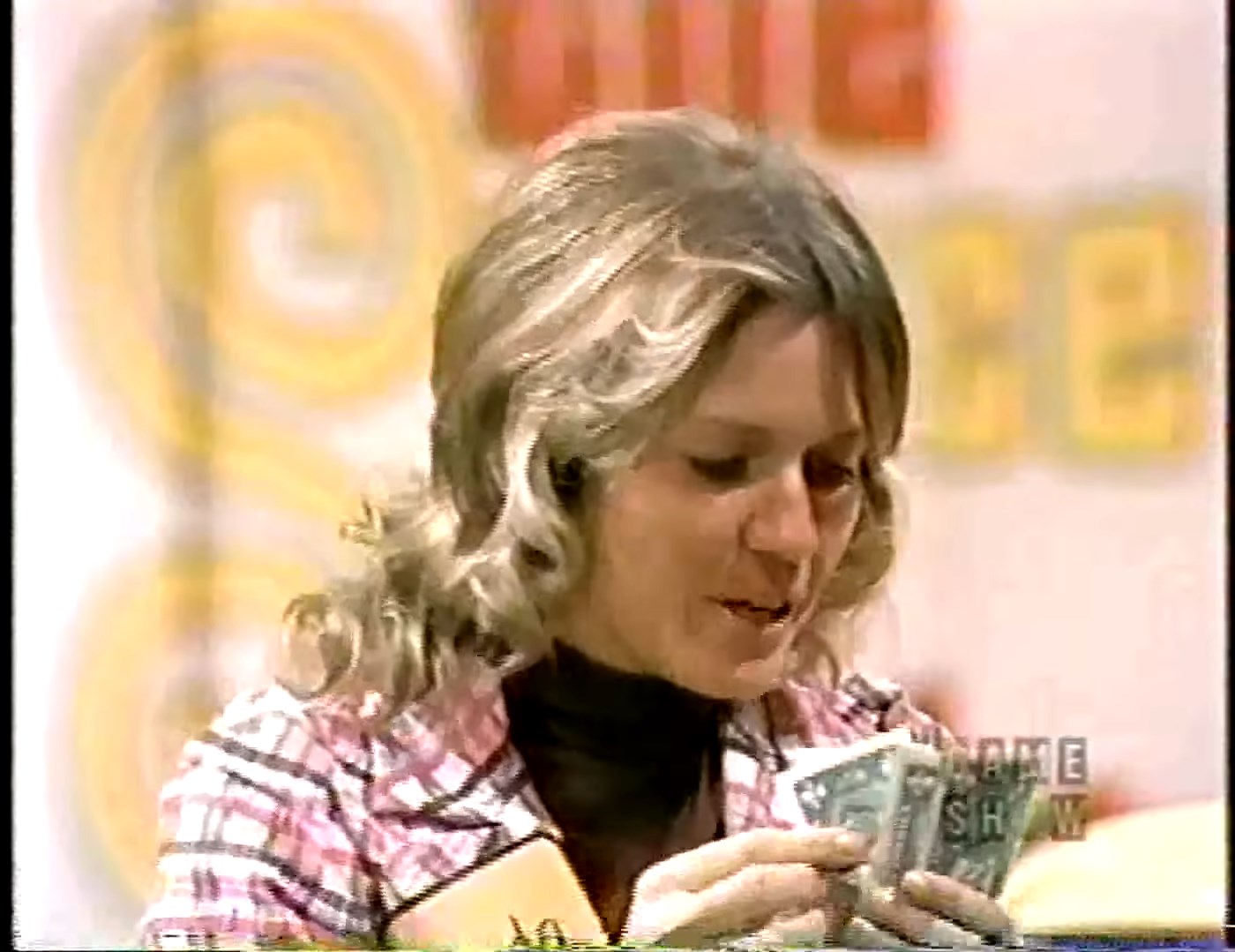 A contestant at a game show holding several dollar bills while looking at them with a focused expression.
