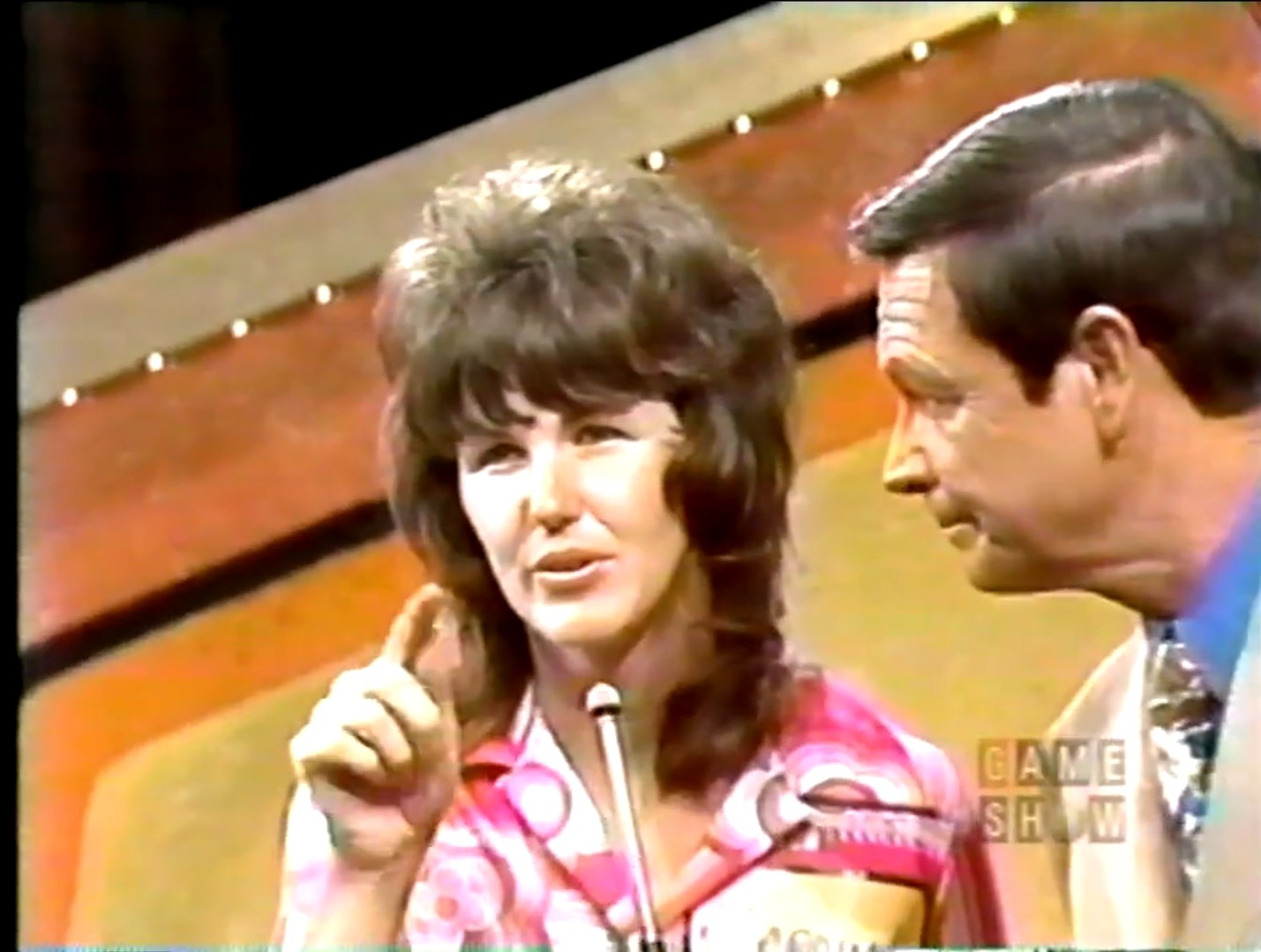 A female contestant in a colorful shirt communicates with a male host during a 1973 episode of The Price is Right.