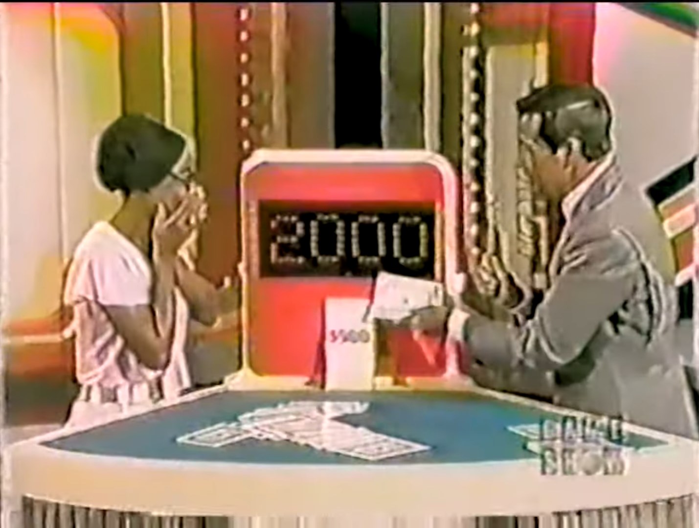 Contestant reacting in surprise while standing next to a game show host, who is revealing a bid of ,000 on a game board.