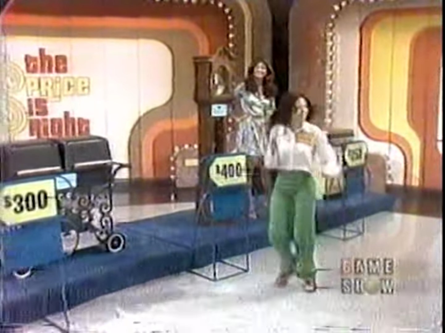 A contestant runs on the stage of 'The Price is Right' during the Race Game, with two price tags visible: 0 and 0, and a vintage clock in the background.