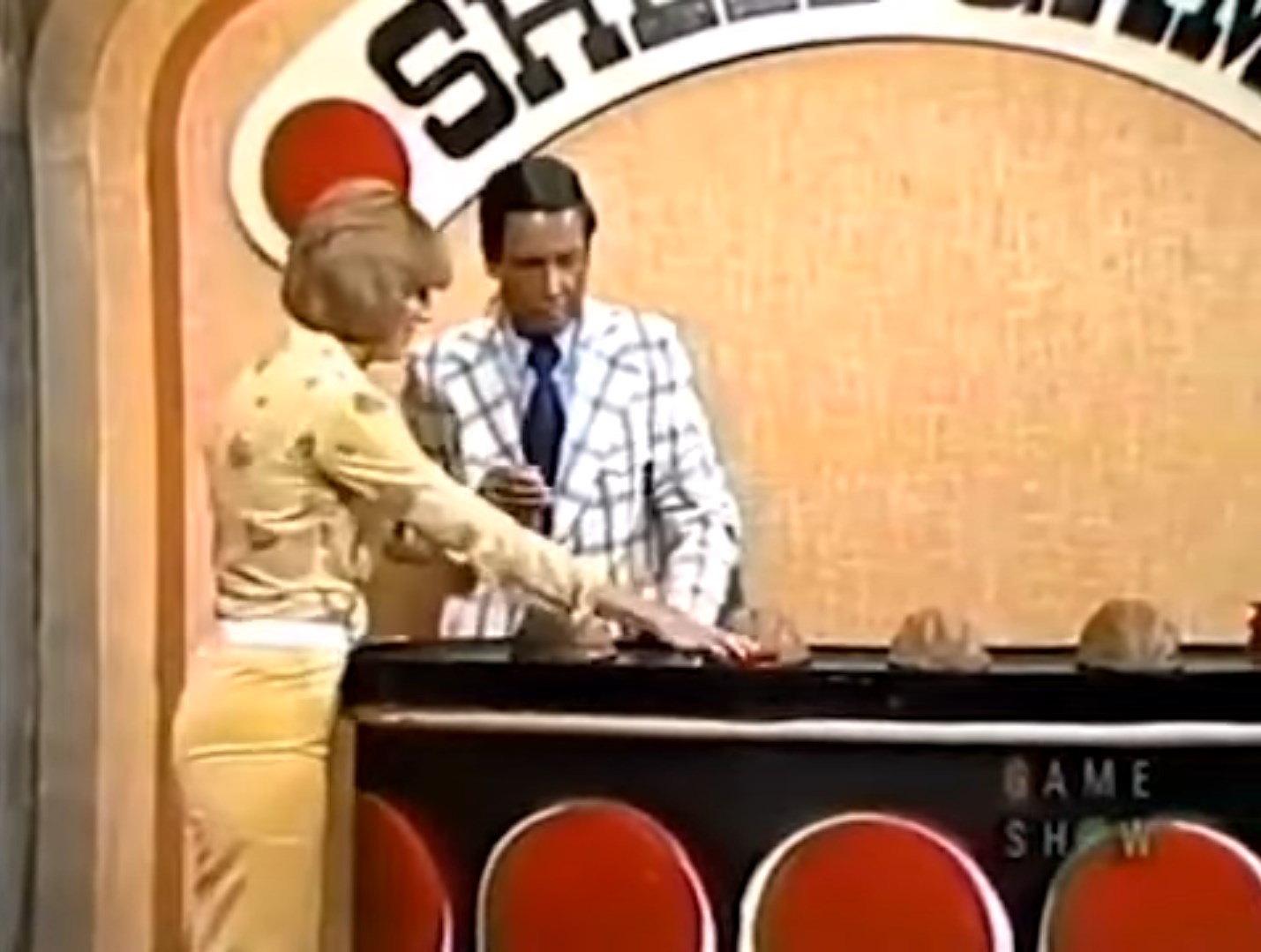 A contestant is playing the Shell Game on stage, mixing shells while the host observes.