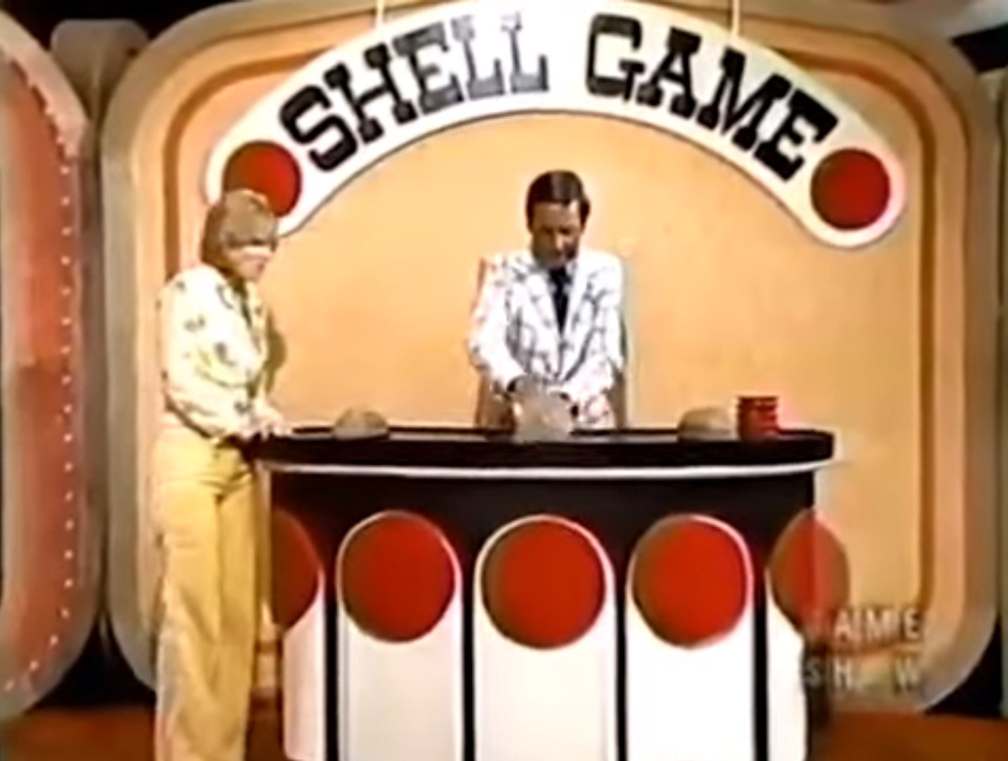 A host is mixing up shells in the Shell Game, on The Price is Right with a contestant observing excitedly.