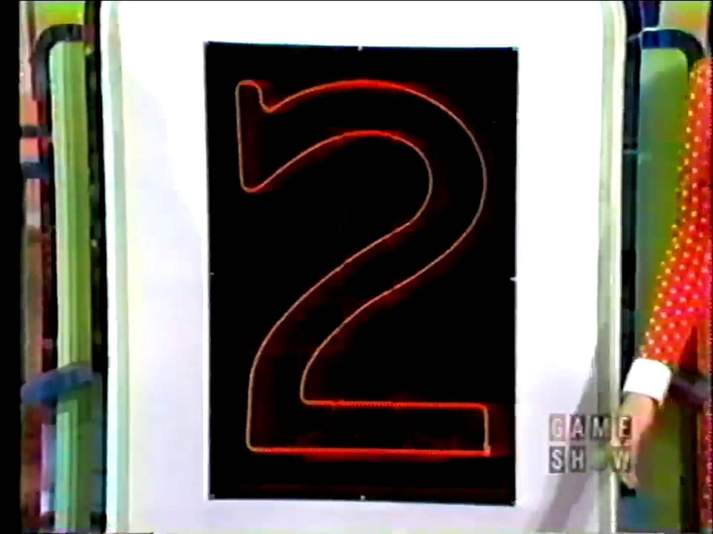 A neon number '2' illuminated against a black background, displayed on a game show set.