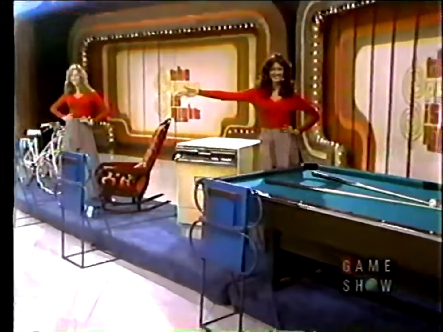 Two models stand beside four prizes: a bicycle, a rocking chair, a dishwasher, and a pool table, set on The Price is Right in 1974.