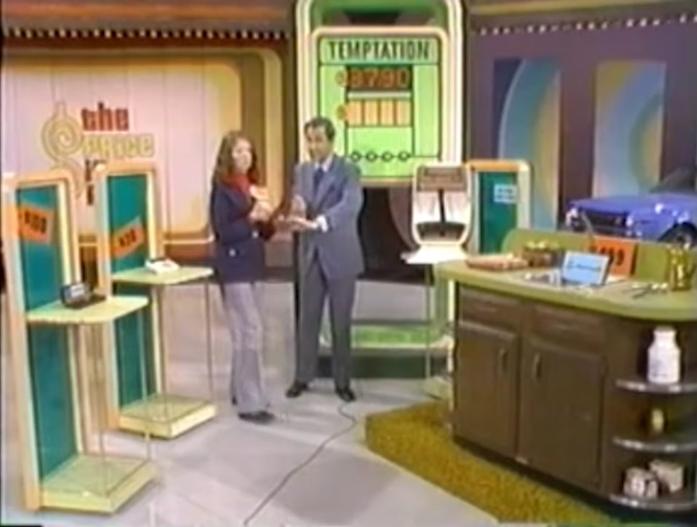 A contestant and host are engaged in the game 'Temptation,' with prizes displayed including a car and several gifts, set against a colorful game show backdrop.