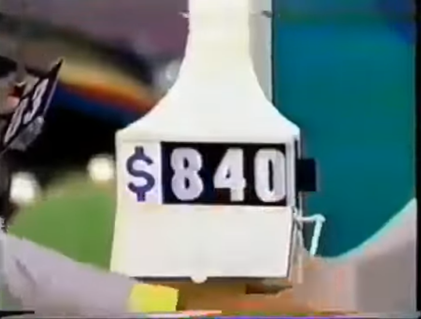 0 is displayed on a pricing game sign during a game show, with a contestant holding a card.