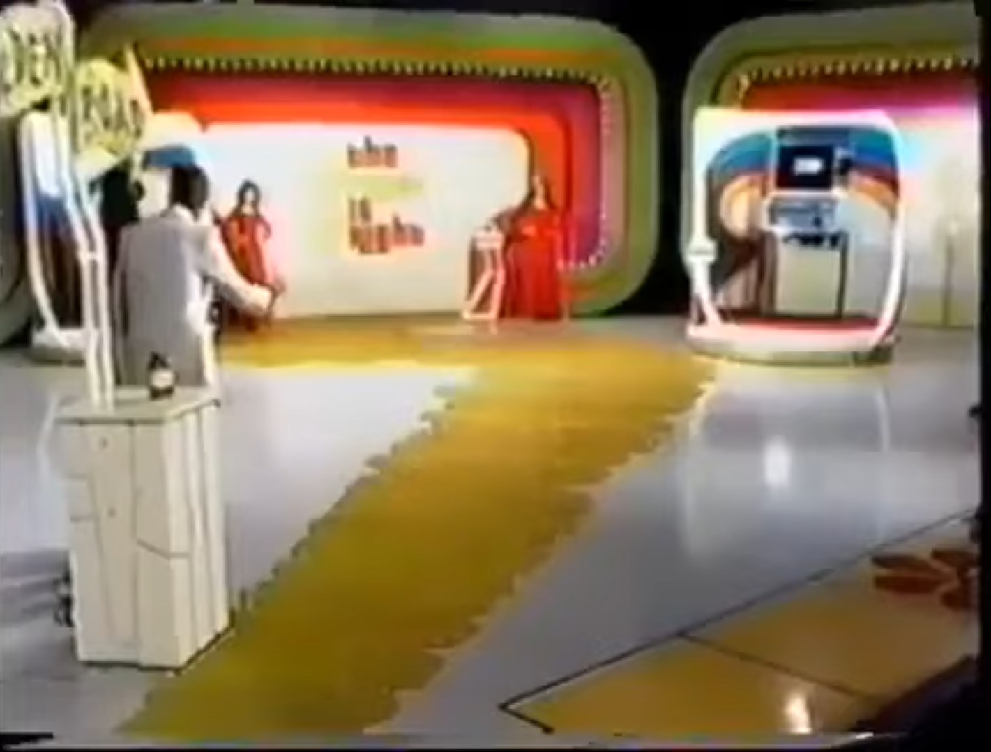 A brightly colored stage setup for the game 'Golden Road', featuring a golden carpet leading to various prize displays, with a host and contestants in the scene.