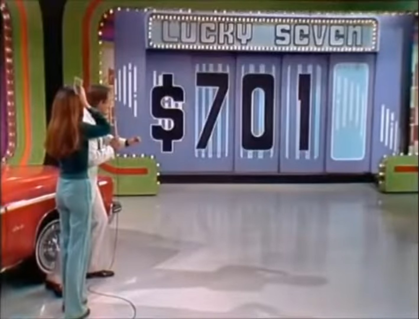 A game show scene with a contestant and host revealing the price of a car in the Lucky Seven game. The displayed price reads 1 against a colorful backdrop.