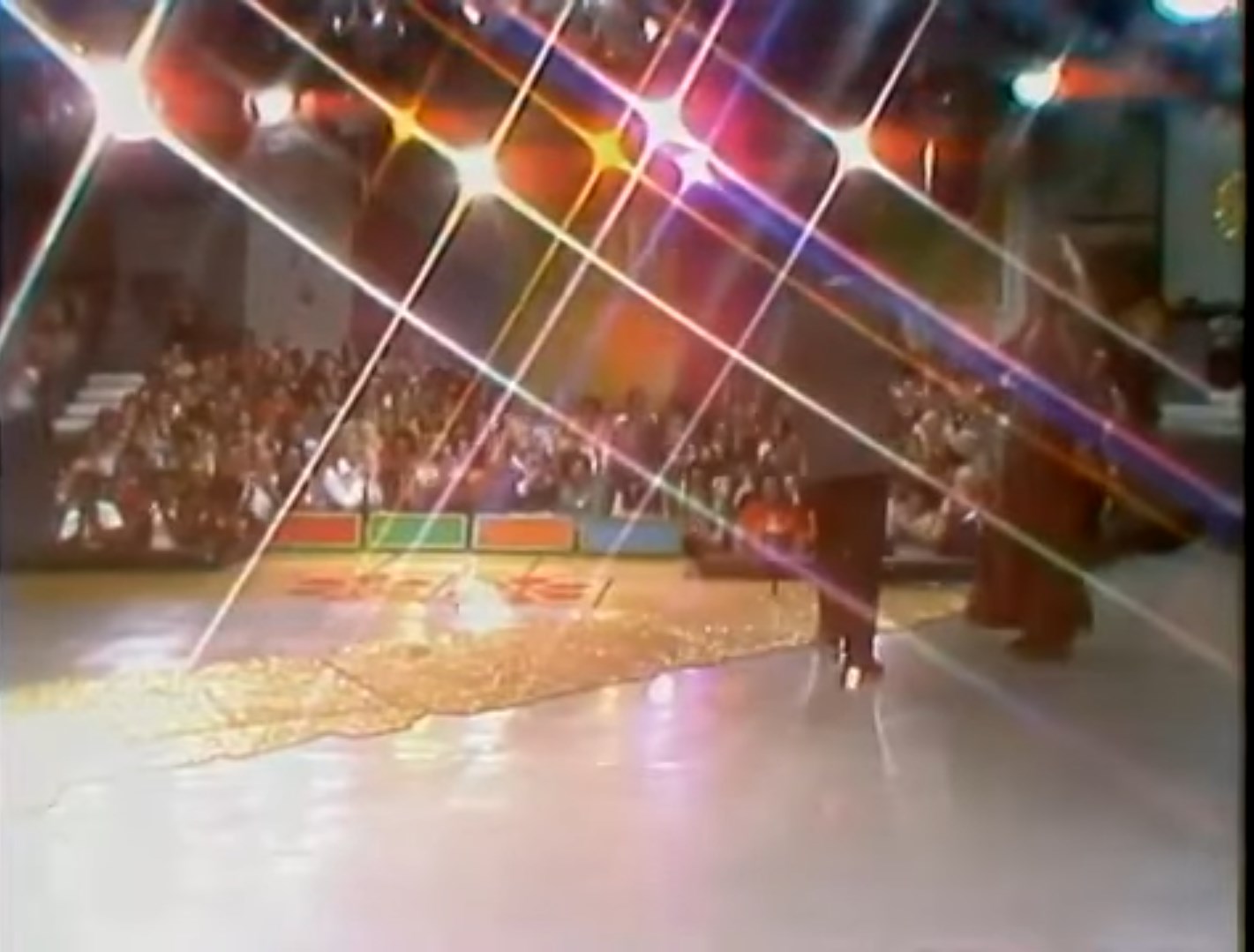 A stage scene from the game show 'The Price is Right' featuring dazzling lights and a glittering golden road, with an audience visible in the background.
