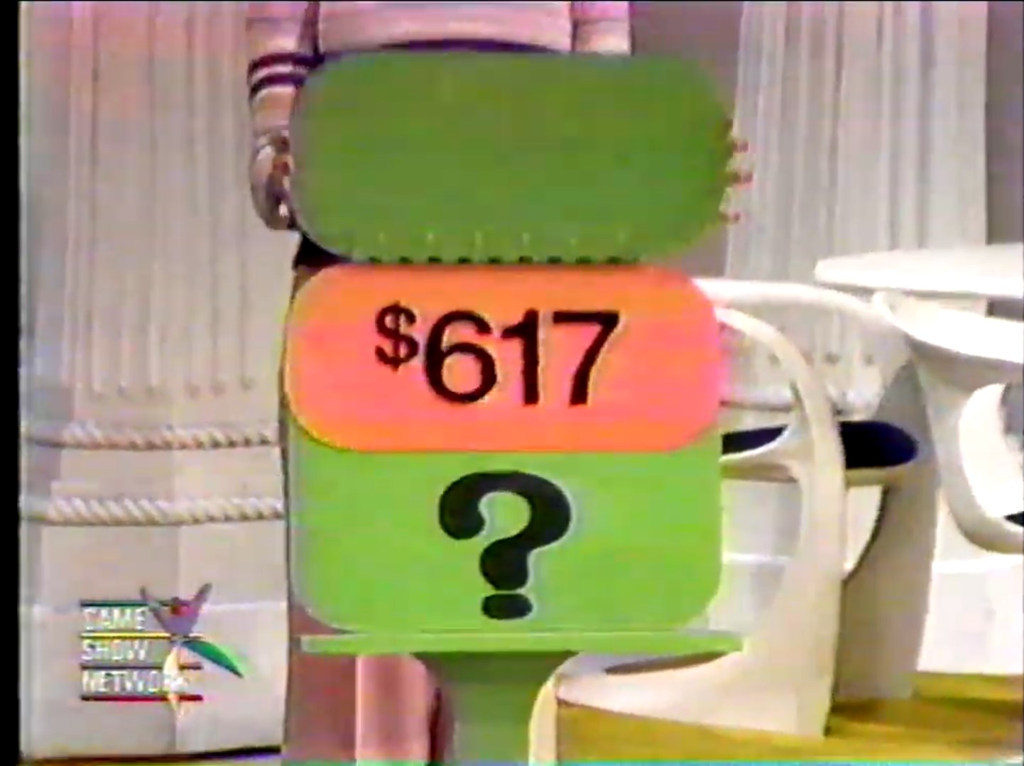 7 displayed on a game show price tag with a green background and a question mark, set against a vintage styled TV studio environment.