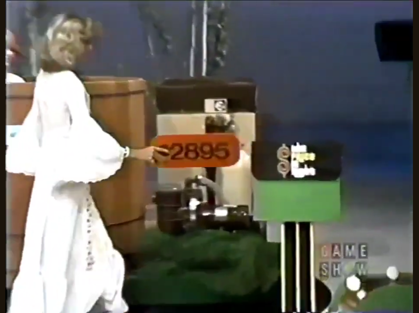 A contestant holds a price tag of 95 next to a prize setup on a game show stage.