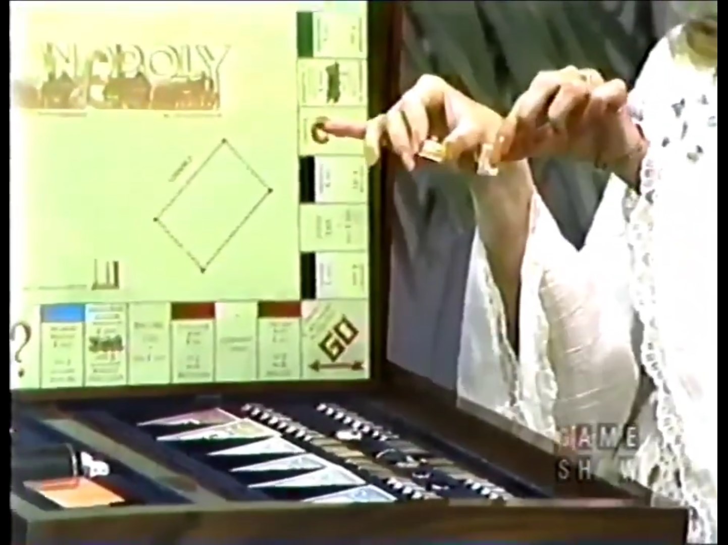 Contestant holds Monopoly game pieces while pointing at the game board.