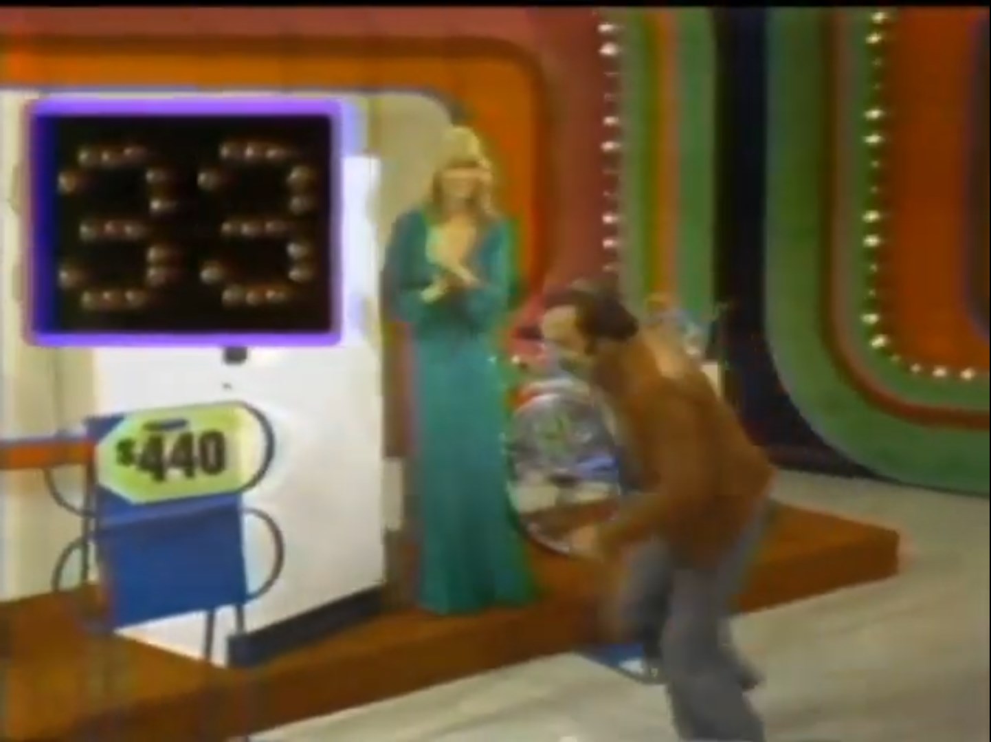 A game show contestant runs toward a price display while a model claps in the background, showcasing the excitement of the Race Game on The Price is Right.