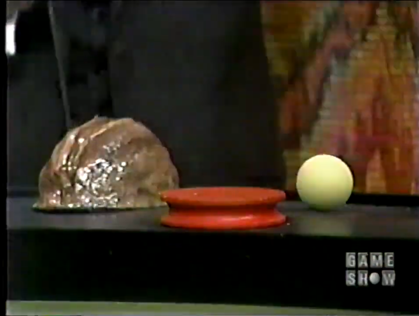 A close-up of a Shell Game setup featuring a shiny shell, a red disc, and a white ball on a black surface.