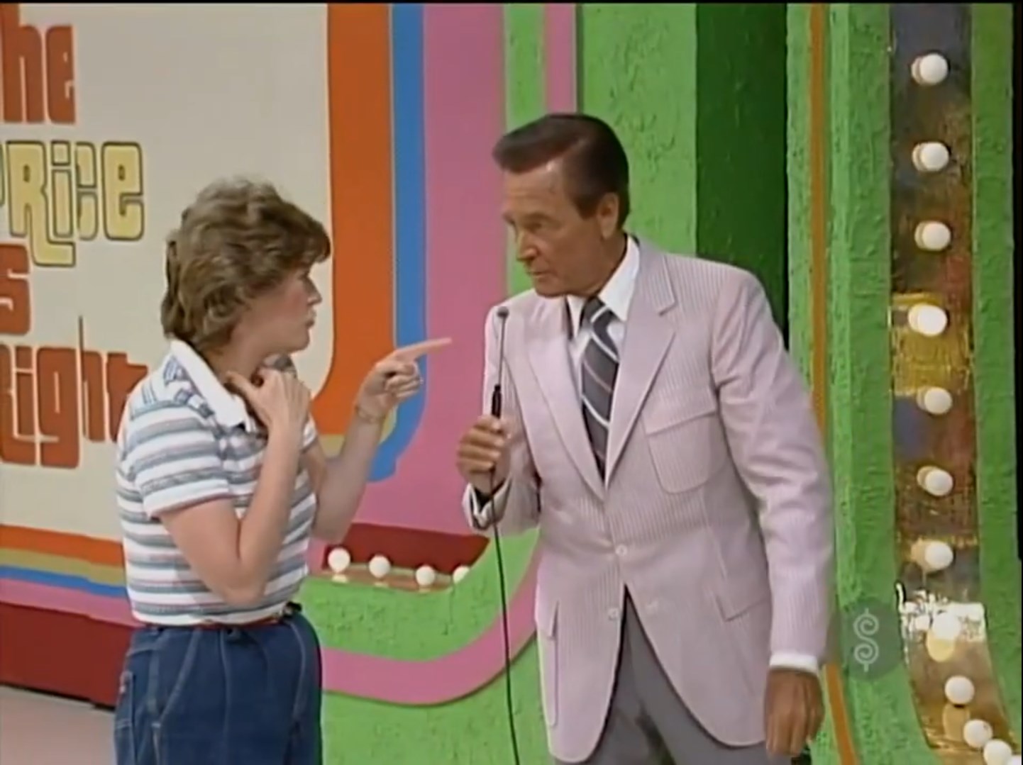A contestant animatedly discusses with the host of The Price Is Right in front of a colorful game backdrop.