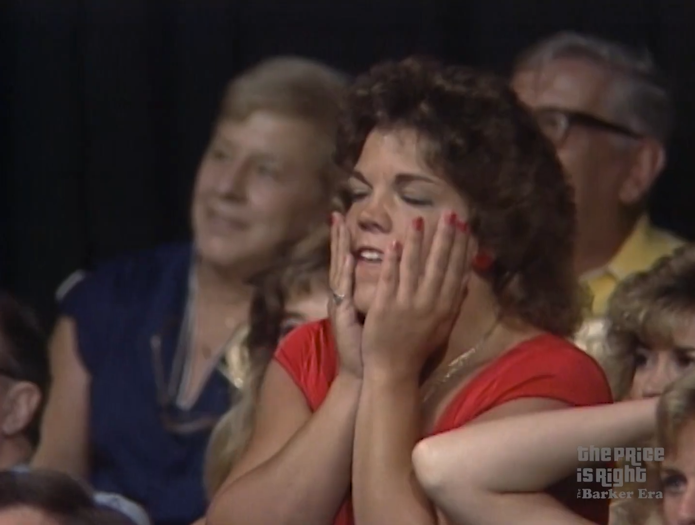 Audience member reacting with excitement and anticipation during a game show, wearing a red top and holding her face in disbelief.