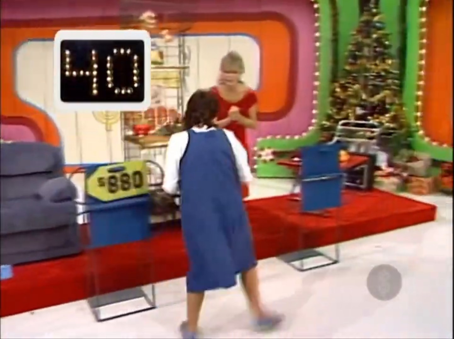 A contestant in a blue dress runs across the stage of The Price is Right, with a timer showing 40 seconds remaining. In the background, a Christmas tree and various prizes are visible.