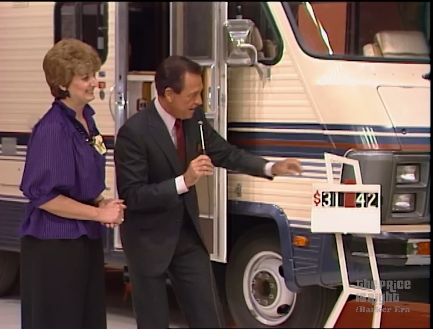 A host interacting with a female contestant next to a large camper, showcasing the price display during a game show.