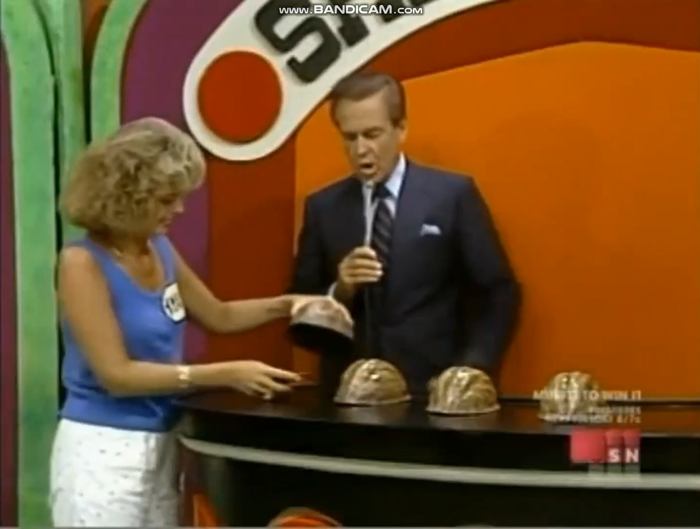 A contestant participates in the Shell Game on The Price is Right, interacting with the game host while examining the shells on the table.